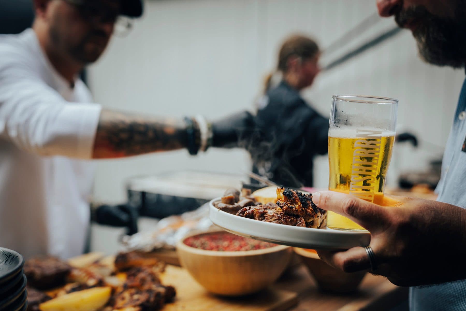 Koch am Grill beim Herzstykke Catering reicht einen Teller